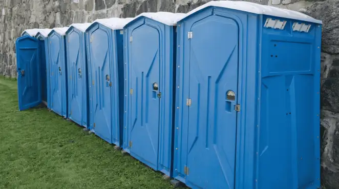 Row of blue portable toilets lined up on grass against a stone wall for event sanitation in Cape Coral, FL